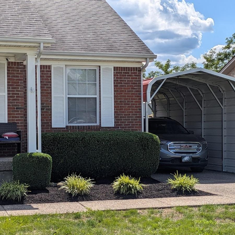A brick house with a carport, its shrubs neatly rounded and a freshly mulched bed with ornamental grasses along the front.